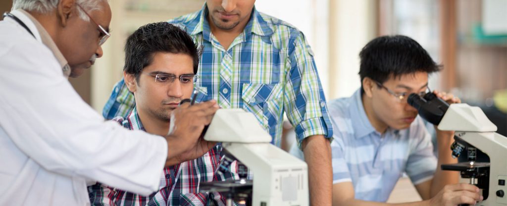 Group of scientists exploring through microscope