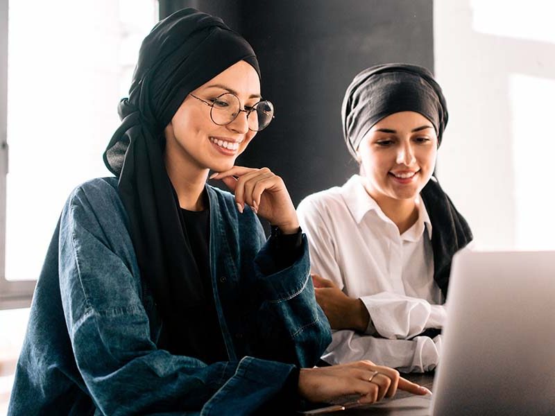 Two Women from the Middle East smile wihle looking at computer