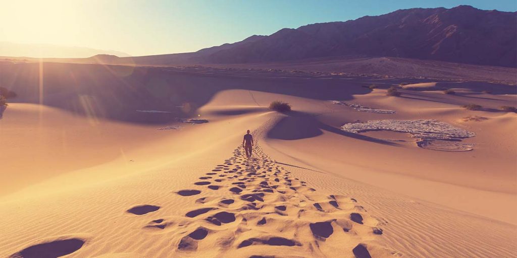 Footsteps from person walking across desert, with sun setting