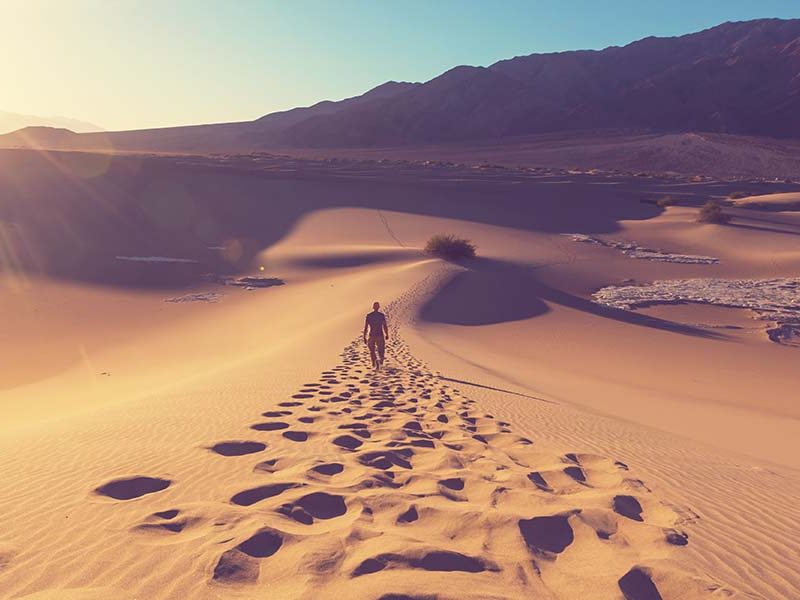 Footsteps from person walking across desert, with sun setting