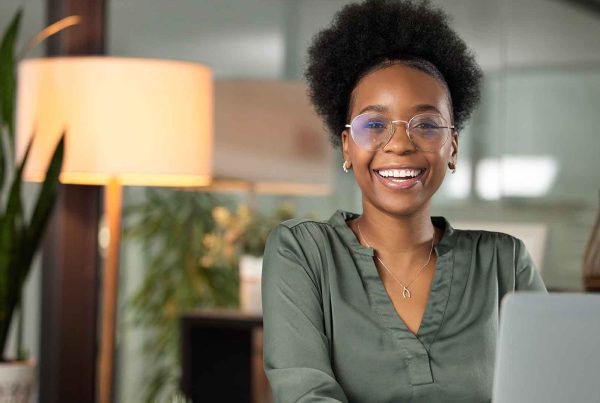 Young woman smiling and looking at camera while working on laptop