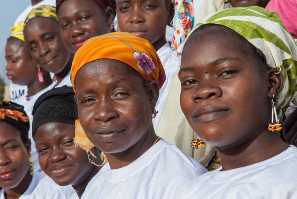 Two lines of Malian women in headscarves and white t-shirts looking at camera