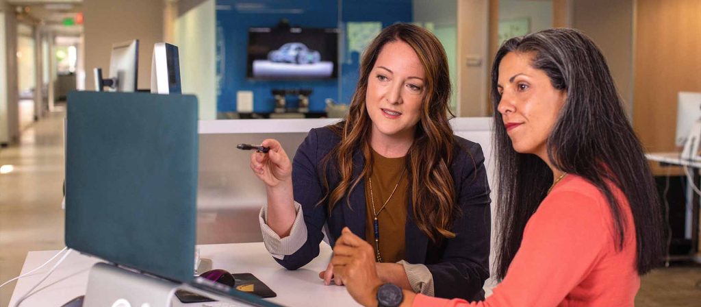 Two business women talking about sales in office at desk with laptop