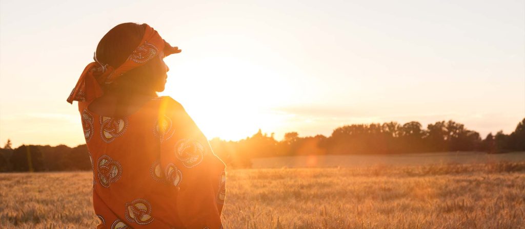 African woman looking across field as sun is setting