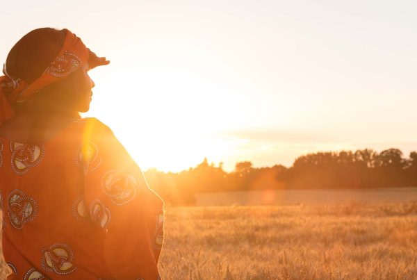 African woman looking across field as sun is setting