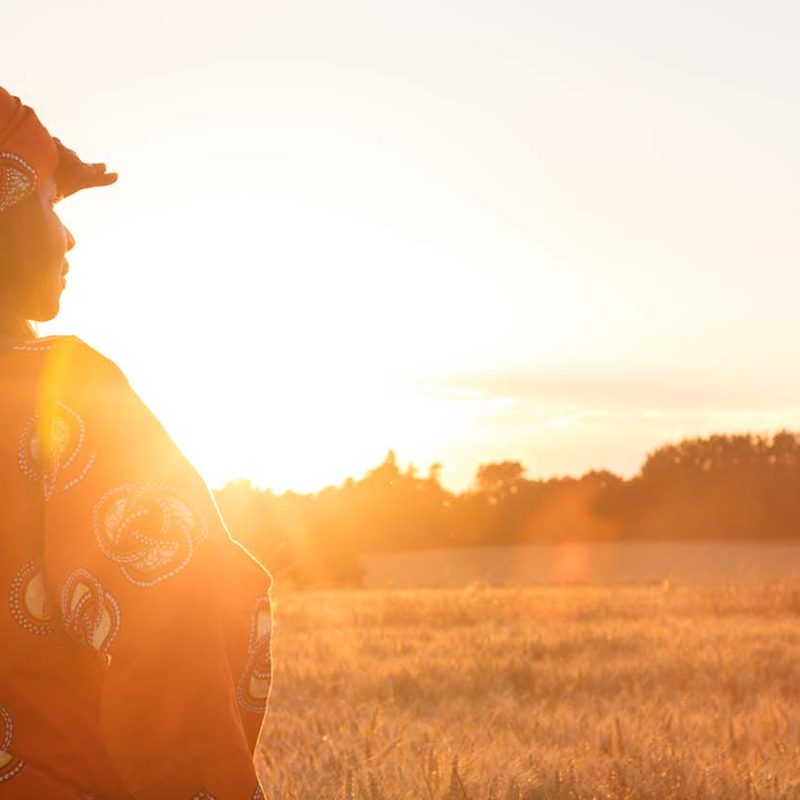 African woman looking across field as sun is setting