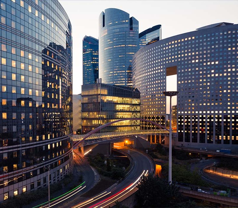 Night architecture. Skyscrapers with glass facade. Modern buildings in Paris business district. Evening dynamic traffic on a street.