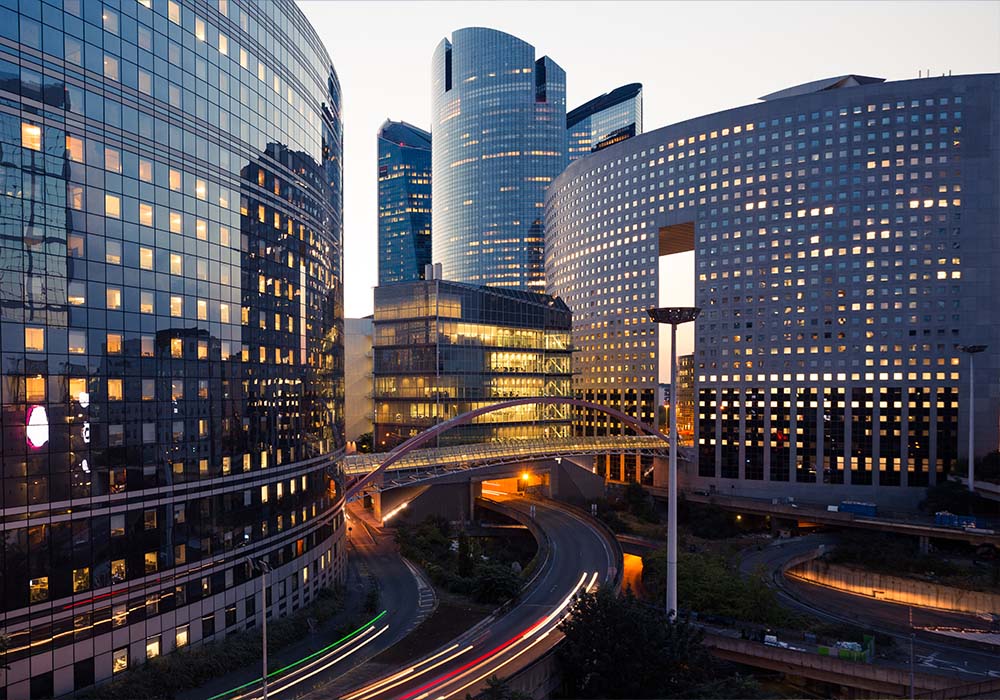 Night architecture. Skyscrapers with glass facade. Modern buildings in Paris business district. Evening dynamic traffic on a street.