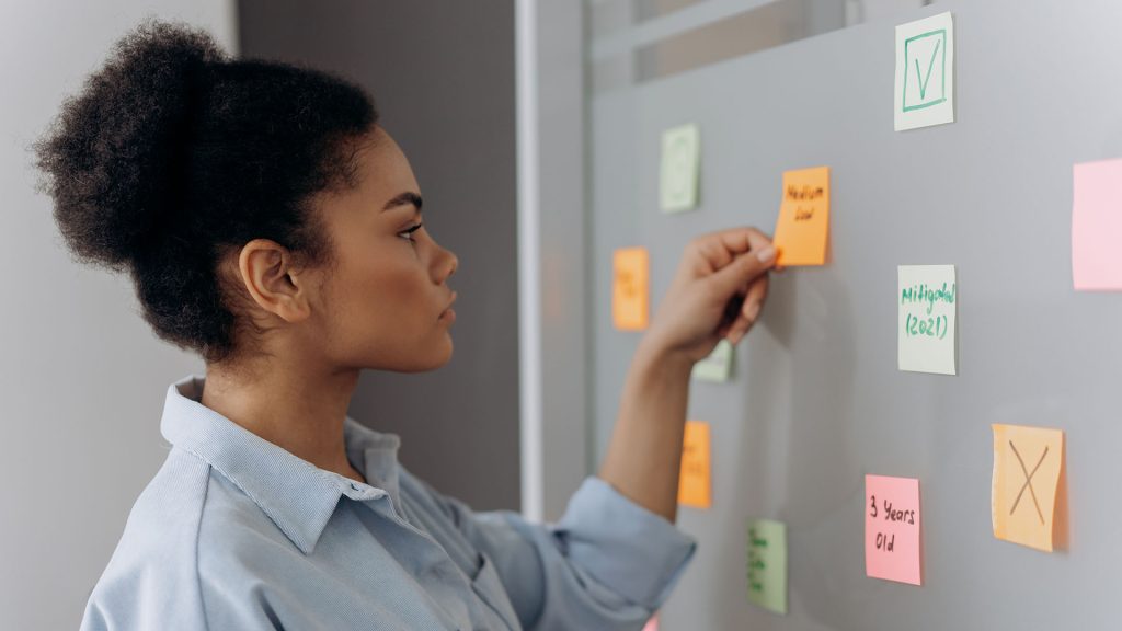 Side view of a woman organizing colorful sticky notes on a whiteboard