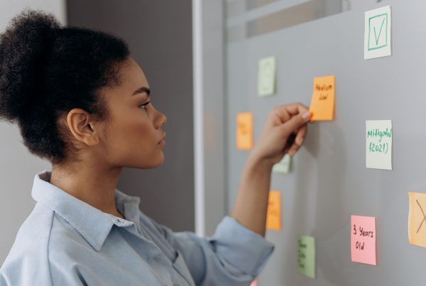 Side view of a woman organizing colorful sticky notes on a whiteboard