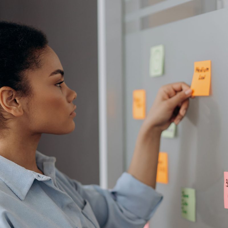 Side view of a woman organizing colorful sticky notes on a whiteboard